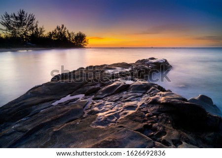 stunning view of sunset at beach with coastal rocks hit by waves. long expose effect may lead to soft focus.
