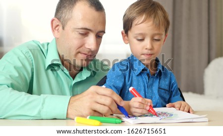 Father and a small boy draw, sitting at the table with colored markers