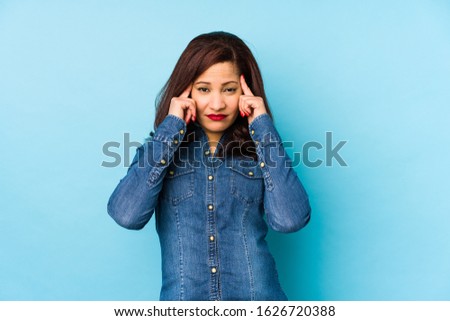 Middle age latin woman isolated on a blue background focused on a task, keeping forefingers pointing head.