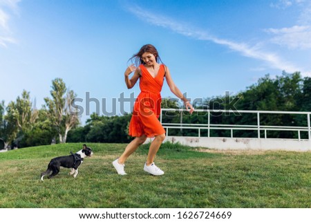 happy pretty woman in park running with boston terrier dog, smiling positive mood, trendy summer style, wearing orange dress, playing with pet, having fun, colorful, active weekend vacation, sneakers