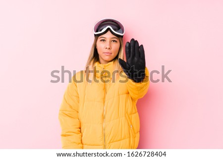 Young caucasian woman wearing a ski clothes in a pink background standing with outstretched hand showing stop sign, preventing you.