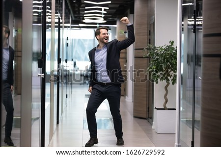 Full length overjoyed young businessman in suit celebrating job promotion. Happy male employee in glasses excited by unbelievable corporate business success, dancing alone in office hallway. Royalty-Free Stock Photo #1626729592