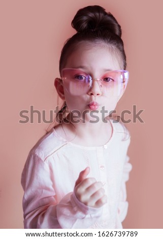 Cute little girl in pink glasses on a pink background. Close-up