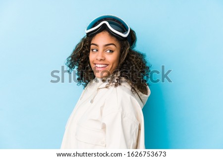 Young african american skier woman isolated looks aside smiling, cheerful and pleasant.