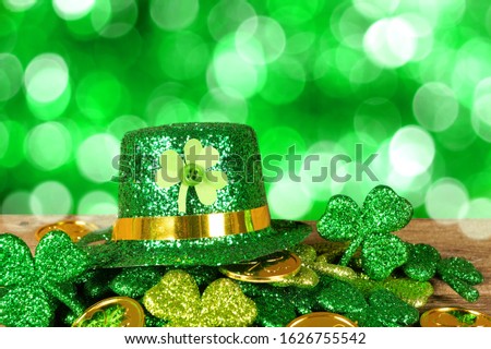 St Patricks Day leprechaun hat on a pile of gold coins and shamrocks in front of a twinkling green background