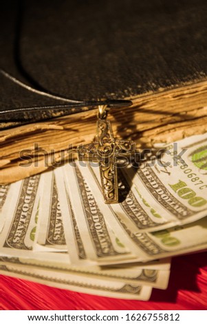 Money in book, church tethe concept. Close up, old vintage holy bible, us dollars and golden cross.