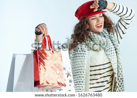 happy elegant woman with long brunette hair in sweater, scarf and red hat with shopping bags isolated on winter light blue background.