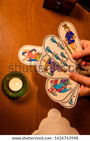 Hands of a mature woman holding divination cards. Pictures are hand-drawn based on old medieval fortune-telling cards.