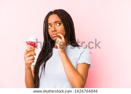Young african american woman holding an ice cream isolated relaxed thinking about something looking at a copy space.