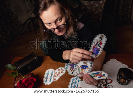 Mature woman guessing on cards to an invisible client. Pictures are hand-drawn based on old medieval fortune-telling cards. Fortuneteller holds a card with a Lady, top view