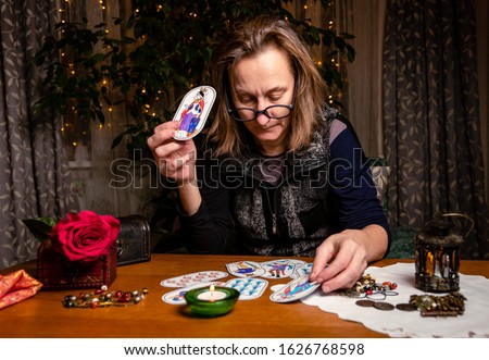 Mature woman guessing on cards to an invisible client. Pictures are hand-drawn based on old medieval fortune-telling cards. Fortuneteller holds a card with a Lady and looks at another cards