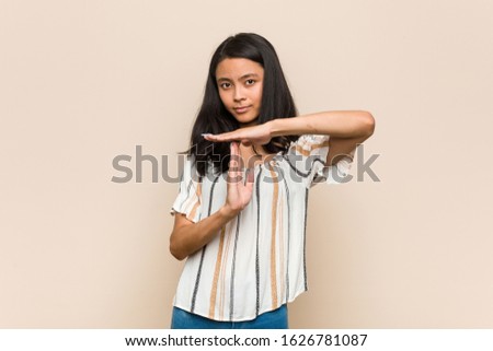Young cute chinese teenager Young blonde woman wearing a coat against a pink background showing a timeout gesture.