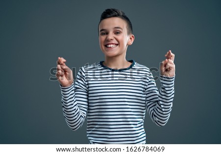 Child crossing fingers. Young man making wish, hopeful, looking up isolated grey wall background. Human face expressions, emotions, feelings, body language, signs, symbols
