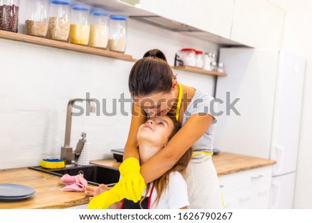 Daughter helping her mother with dishwashing in the kitchen, thankful mother hugs her, kissing on the forehead.