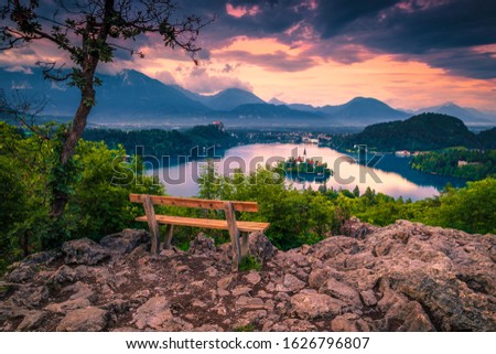 Picturesque resting place with wooden bench on the top of mountain. Panoramic view with lake Bled and small island at sunset, Slovenia, Europe