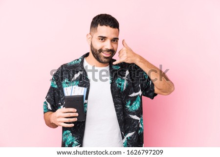 Young arabian cool man holding a boarding passes isolated showing a mobile phone call gesture with fingers.