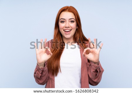 Redhead teenager girl over isolated blue background showing an ok sign with fingers