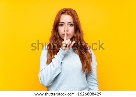 Teenager redhead girl over isolated yellow background showing a sign of silence gesture putting finger in mouth