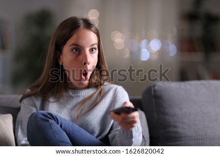 Surprised woman watching tv sitting on a couch at home in the night Royalty-Free Stock Photo #1626820042