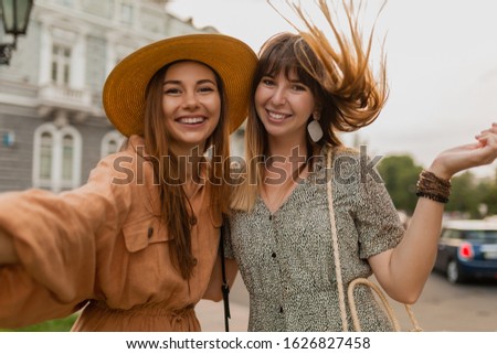 stylish young women traveling together in Europe dressed in spring trendy dresses and accessories smiling happy friends having fun taking selfie photo on camera