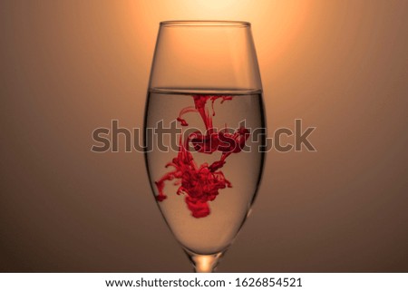 Red food coloring diffuse in water inside glass , with gradient background