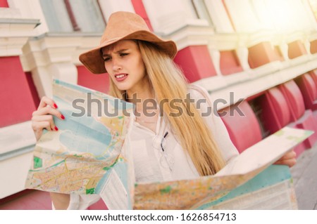 Young casual style tourist woman in felt hat looking into the city map against the background of old urban architecture. The concept of travel to unfamiliar cities