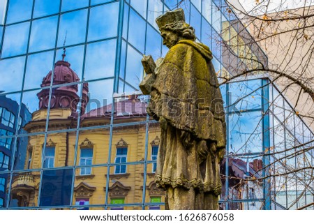 Sculpture of a holy minister, against the background of a modern building made of glass.