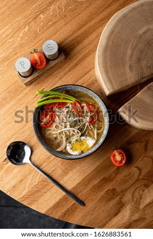 Top vie of chicken noodle soup with boiled egg, tomatoes and chili pepper on wooden table