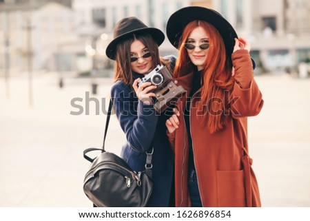Two happy pretty young best friends, hugs smiling laughing and having funny crazy time together, wearing stylish retro vintage feminine clothes. Outdoors.