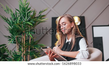 Beauty young woman in glasses siting in the office with tablet, generating ideas. Plants on the background. Business and education