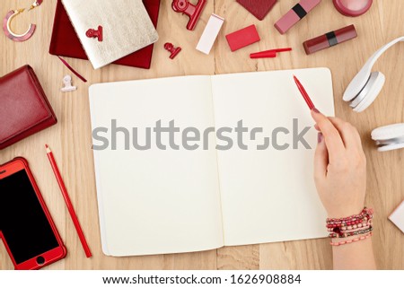 Mock up woman hand writing in empty notebook and red office stationary. Flat lay, top view. Journal day planing, drawing, making notes mockup. Creativity, home office concept