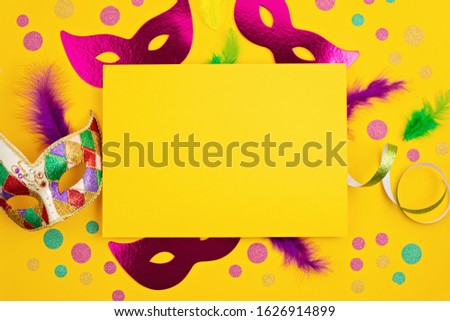 Festive, colorful mardi gras or carnivale mask and accessories over yellow background. Party invitation, greeting card, venetian carnivale celebration concept. Flat lay, top view, copy space