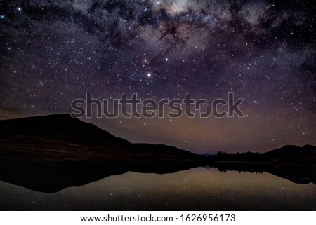 A galaxy of stars and the milky way reflected on a mountain lake with silhouetted  hills in the background