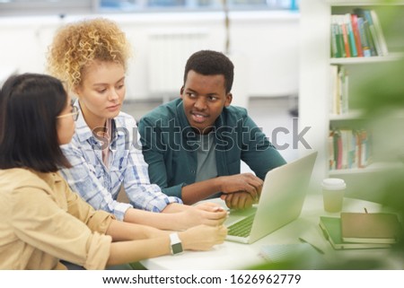 High angle portrait of multi-ethnic group of students using laptop together while working on project in library, copy space