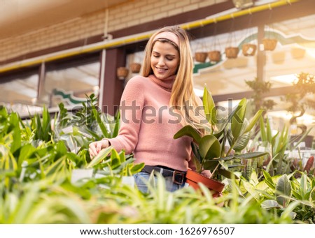 Worm eye view pretty girl smiling while choosing plants in store 