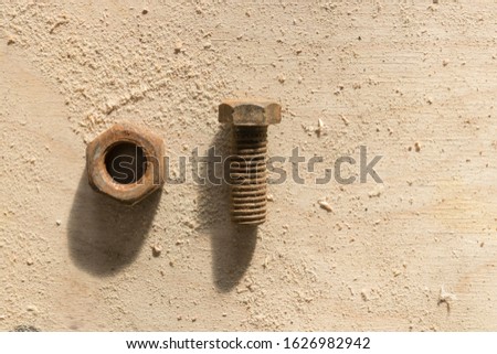 Old rusty nut and bolt lie on a dusty wooden table (blurred) in the light of the bright day sun with a sharp shadow