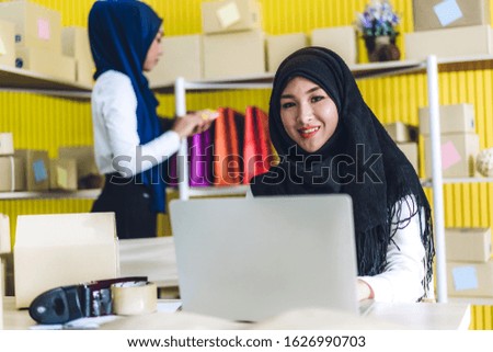 Muslim two asian woman freelancer sme business online shopping working on laptop computer and checklist order with cardboard box on table at home - Business online shipping and delivery concept