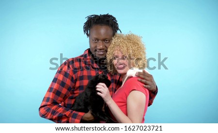 a pair of African male and a Caucasian woman together. holding a black cat and a white rat. blue background.