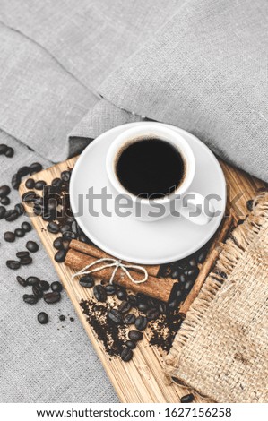 Coffee white cup and saucer on a wooden board with coffee beans and cinnamon on a gray linen tablecloth. Good morning
