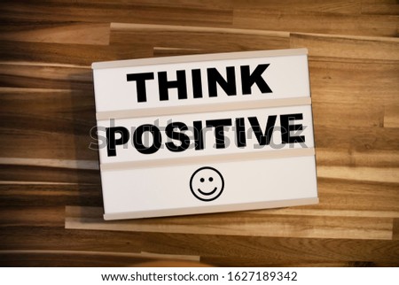 Lightbox or light box with happy smiley and message Think positive on a wooden table