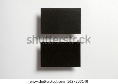 Two black blank glossy textured business cards flying and isolated over the white paper background, 
UK standard size 85 mm x 55 mm, professional studio photo.
