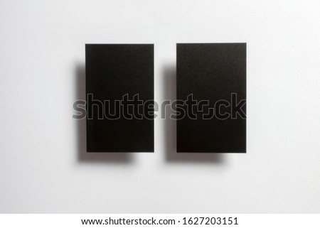 Two black blank glossy textured business cards flying and isolated over the white paper background, 
UK standard size 85 mm x 55 mm, professional studio photo.