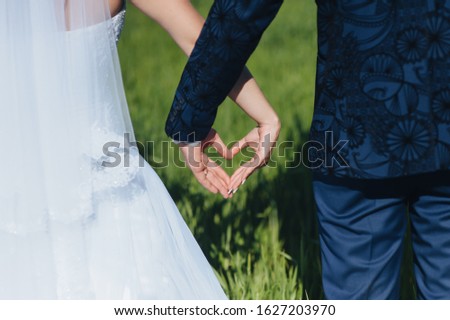 Stylish groom in a blue suit and a beautiful bride in a white dress show with hands, fingers a symbol of heart and love. Photography, concept.