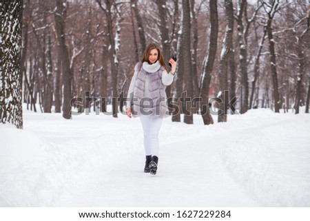 Close up portrait of a young beautiful girl in fur vest walking in a winter park