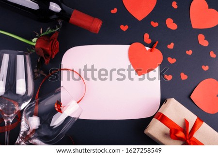 Valentine's day greeting card with wine glasses, bottle of wine and gift box on black background. Top view with space for your greetings. Flat lay