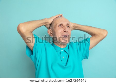 Holding head in hands, shocked. Caucasian senior man's portrait on blue studio background. Beautiful male emotional model. Concept of human emotions, facial expression, sales, wellbeing, ad. Copyspace