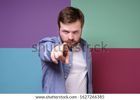 Bearded man with a stern look, makes a stop gesture with his index finger and tries to calm someone.