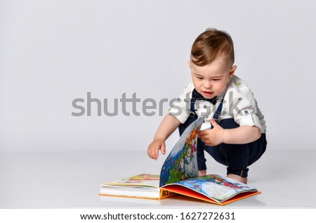 Little boy kid turns the page in the book with colorful pictures. He is very happy and excited about viewing photos. Child concept Isolated on white background