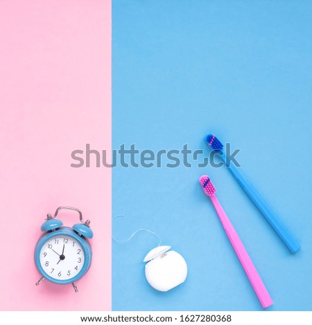 Teeth hygiene and oral dental care products and alarm clock on color pink and blue background copy space. Blank tube of dental floss and brushes. Flat lay top view composition, mockup. Morning concept