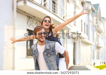 Handsome young man carrying young attractive woman on shoulders while spending time together outdoors.